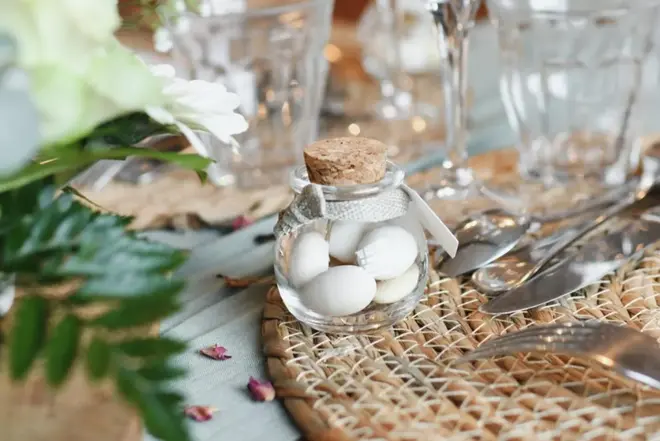 Small glass jars filled with white candies on a woven placemat at a wedding reception table