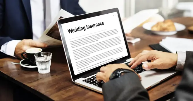 Couple reviewing wedding insurance paperwork together at a table with wedding planning materials